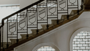 Barandilla de hierro en una escalera interior, con paneles decorativos geométricos y pasamanos negro.